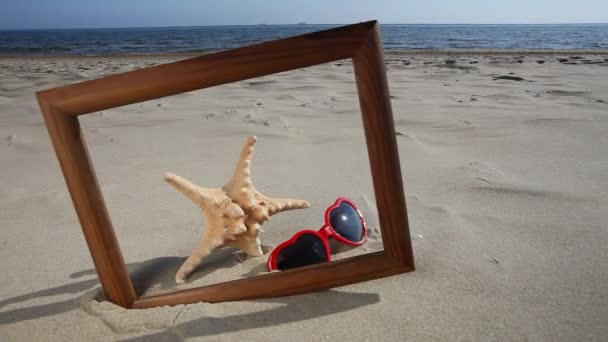 Concha, estrella de mar y gafas en marco de madera en la playa — Vídeos de Stock