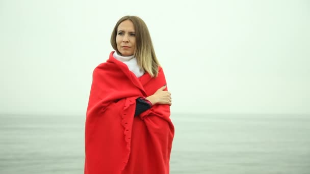 Sad woman standing on the shore nestled in red plaid — Stock Video