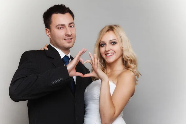 Portrait of happy bride and groom showing heart sign — Stock Photo, Image