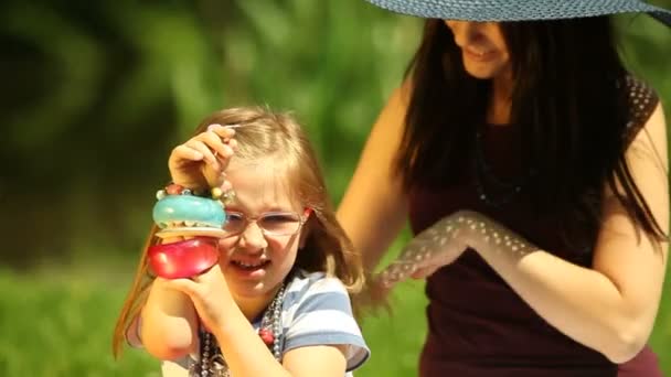 Jonge moeder in stro hoed kammen dochter op de weide of in het park — Stockvideo