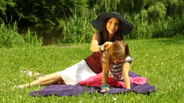 Jeune mère en chapeau de paille peigner fille sur la prairie ou dans le parc — Video