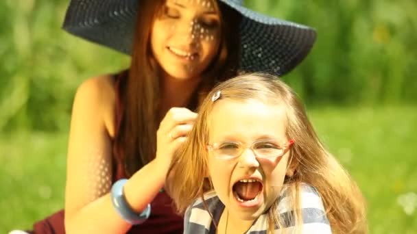Мама в соломенной шляпе с маленькой дочерью отдыхает на лугу или в парке — стоковое видео