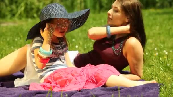 Mutter mit kleiner Tochter im Strohhut und Brille entspannt auf der Wiese oder im Park. — Stockvideo