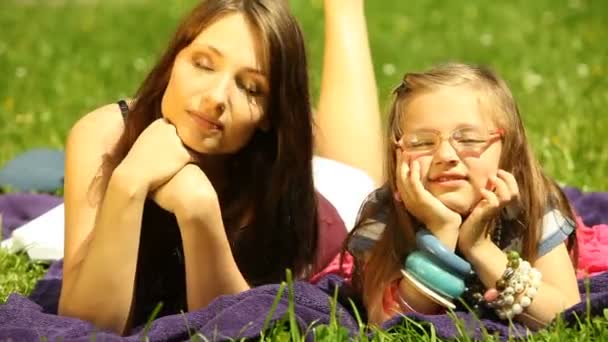 Mutter mit kleiner Tochter im Strohhut und Brille entspannt auf der Wiese oder im Park. — Stockvideo