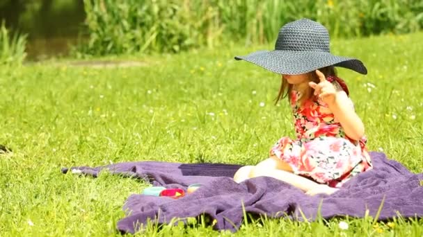 Маленькая девочка в черной соломенной шляпе на лугу или в парке на открытом воздухе . — стоковое видео