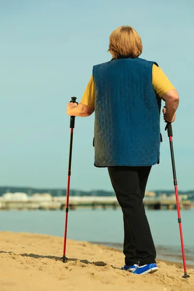 Mujer activa sénior nórdico caminar en una playa. desde atrás —  Fotos de Stock