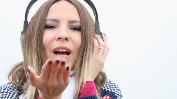 Šťastný Glamour girl mladá žena s sluchátka, poslech hudby, foukání pusu a spiklenecky venkovní — Stock video