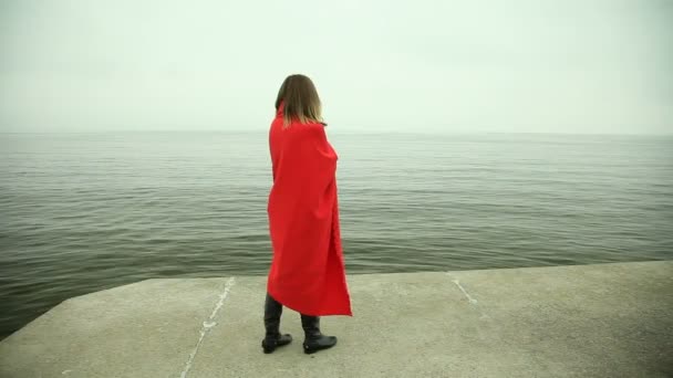 Chica solitaria en manta roja mirando al mar o al océano — Vídeos de Stock