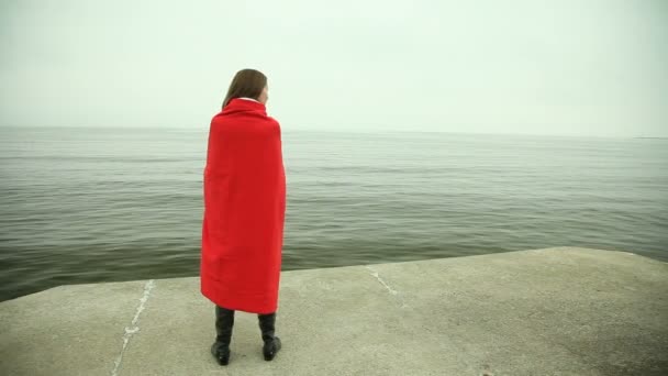 Sad pensive woman in red blanket standing on the sea shore — Stock Video
