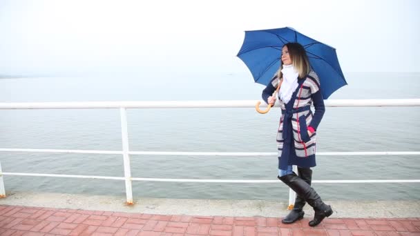 Mujer joven con paraguas azul relajándose en el muelle en días lluviosos — Vídeos de Stock