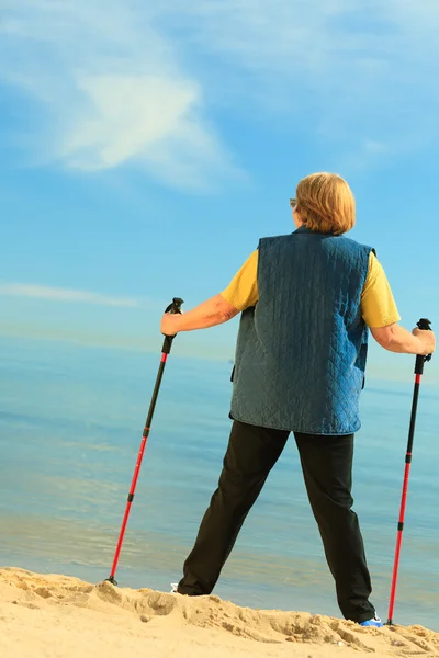 Žena starší nordic walking na pláži — Stock fotografie