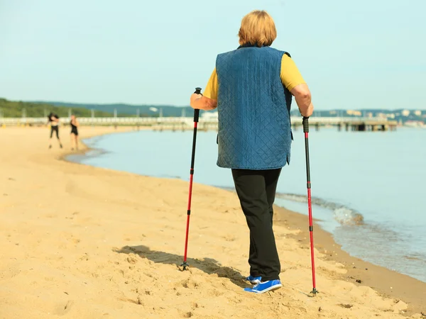 Active woman senior nordic walking on a beach. from behind — Stock Photo, Image