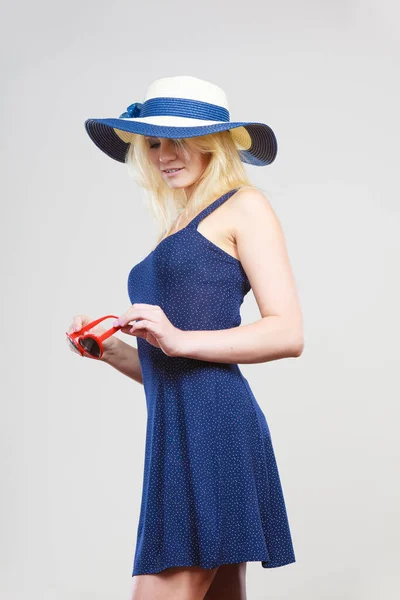 夏季新潮时髦的衣服创意概念 金发美女穿着短蓝色晚礼服和太阳的帽子 太阳镜 坚持灰色 — 图库照片