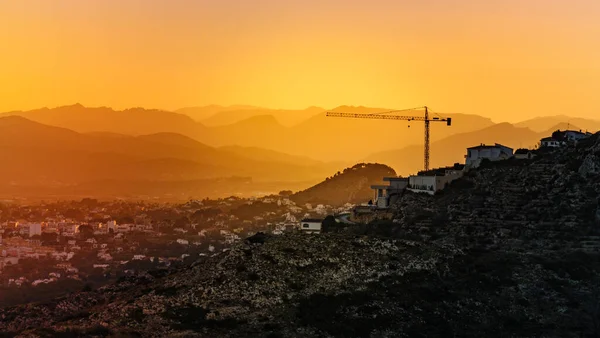 丘の上にクレーン産業機器と建設現場とスペインの海岸の風景の上に夕日 建物活動 — ストック写真