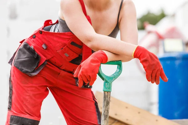 穿着工装裤在建筑工地上用大铲子工具工作的难以辨认的迷人女人 — 图库照片