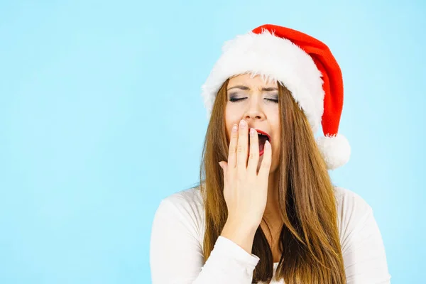 サンタの帽子をかぶった疲れた女性があくびをしている 大人の女性は 昼寝をする準備ができて眠いです クリスマスタイム — ストック写真