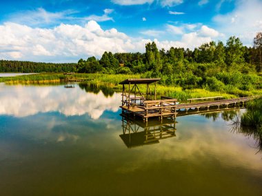Green summer landscape in Europe. Wooden jetty on shore of Lake Kierwik in Masuria Poland. Blue sky retlected in water. Aerial view clipart