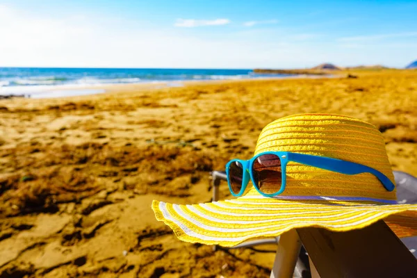 夏と休日は 海辺で休んでいます 砂浜の海岸で青いサングラスと黄色の麦藁帽子 — ストック写真