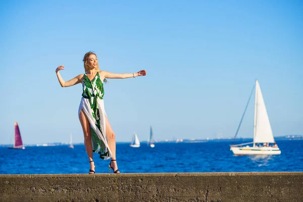 Beautiful fashion model against sea. Pretty blonde young adult woman wearing long white green summer dress.