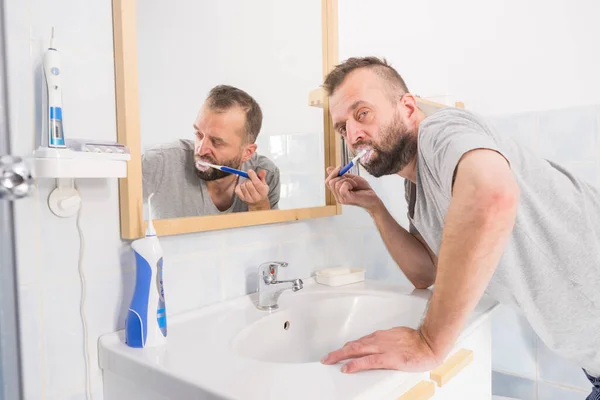 Adult man brushing his teeth looking at his bathroom mirror during morning hygiene routine.