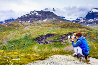 Tourist woman enjoy mountains landscape, taking travel photo with camera. National tourist scenic route 55 Sognefjellet, Norway clipart