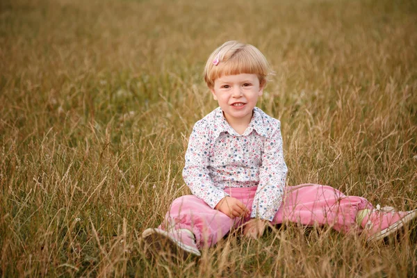 Liten flicka sitter i gräset — Stockfoto