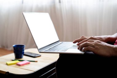 Evdeki dizüstü bilgisayarını kullanan ve daktilo kullanan bir adamın maketi. boş beyaz masaüstü ekran ile
