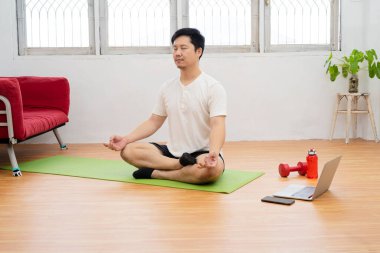 Cihazlarla çevrimiçi eğitim. Akıllı saati olan adam yoga yapıyor, gündüz evde eğitim videosu izliyor, boş yer var.