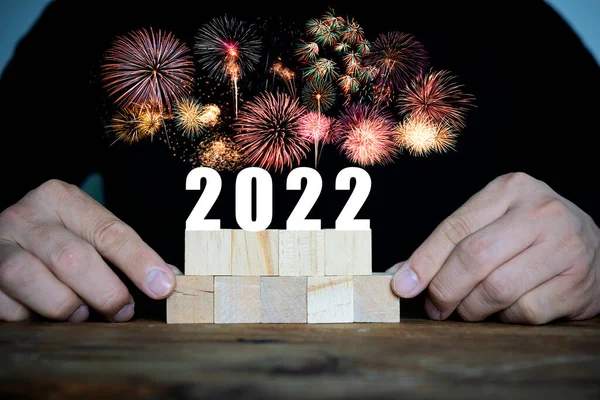 木製のブロックを保持男性の手は机の上に配置され 番号2022新年は美しい花火で祝われます — ストック写真