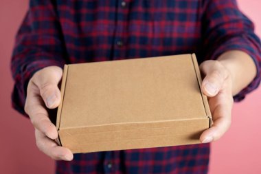 Teslimatı yapacak teslimatçının elleri. Gri arka planda kahverengi kutuyu tutan kurye. Fotokopi alanı etiketli karton paket taşıyan teslimatçının ayrıntıları.