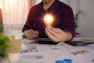 İş adamı hesap makinesi kullanarak ampulü tutuyor. Ofis kavramında enerji ve muhasebe tasarrufu fikri