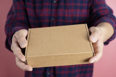 Teslimatı yapacak teslimatçının elleri. Gri arka planda kahverengi kutuyu tutan kurye. Fotokopi alanı etiketli karton paket taşıyan teslimatçının ayrıntıları.