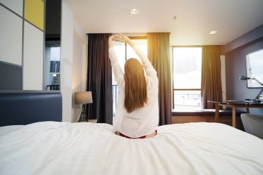 Bir kadın uyandıktan sonra yatakta geriniyor. Yatakta esneme hareketleri. Mutlu Genç Kız Sıcak Güneş Işığıyla Yeni Günü Kutluyor.