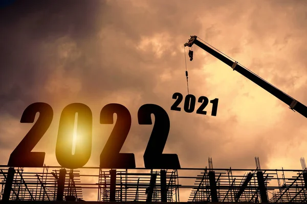 歓迎の準備のためのクレーンと曇りの空と建設労働者のシルエット2022新年会と新しいビジネスを変更します — ストック写真