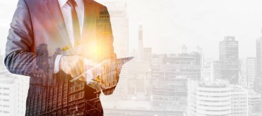 İnşaat işçisinin tablet bilgisayarlı ve inşaat üniformalı halinin görüntüsü şehirdeki sürreal inşaat alanının arka planına karşıdır..