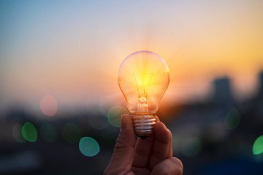 İnsan eli günbatımında bir ampul tutar. Yenilenebilir enerji. Elektrik yeniliği.