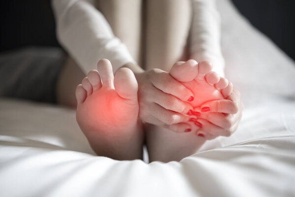 pain in the foot, girl holds her hands to her feet, foot massage, cramp, muscular spasm, red accent on foot, black and white photo, close-up