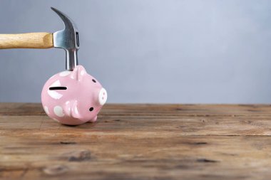 Bir pembe Çin kumbara, şok ve endişeli bir yüz ifadesi ile yukarıda kaldırdı çekiç tutan bir el. Yansıtıcı yüzey ve hafif gri arka plan. Kopya alanı sola.