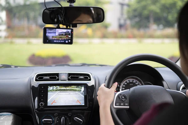 Woman driving in reverse and using a rear view camera in her car to help her reverse safely.