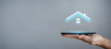 İş adamı ev ikonunu tutuyor. Marketin ev kontrollü, akıllı ev ve ev otomasyon uygulaması konsepti. PCB tasarımı ve akıllı telefonu olan kişi. Yenilik teknolojisi internet ağı kavramı