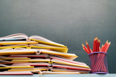 Sınıftaki çalışma masasının açılır kapanır görünümü kitaplarla, karatahta arkaplanlı kırtasiye malzemesi