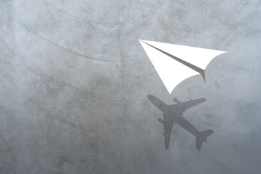 Paper plane in mid flight with shadow of a real plane. Cement texture surface of wall loft style background.