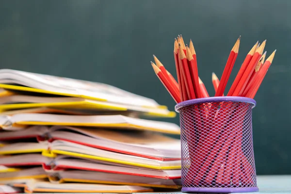 Concept to teacher\'s day. Pens, pencils, books on table, against the background of chalkboard. Back to school, copy space.