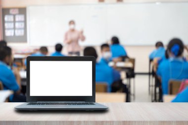 Masadaki bilgisayar, arka plan olarak sınıfın bulanık görüntüsü..