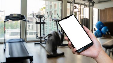 Spor salonunda el ele tutuşan akıllı telefon cihazı. Modern spor salonunun içi ekipmanlarla dolu.