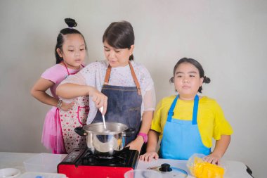 mutfakta mutlu bir aile. genç asyalı anne ve çocuk kızı doğum günü için hamur fırında kurabiye hazırlanıyor. anne ile sevimli çocuk evde kase birlikte un ve yumurta karışımı. zarif kadın kız bakmak
