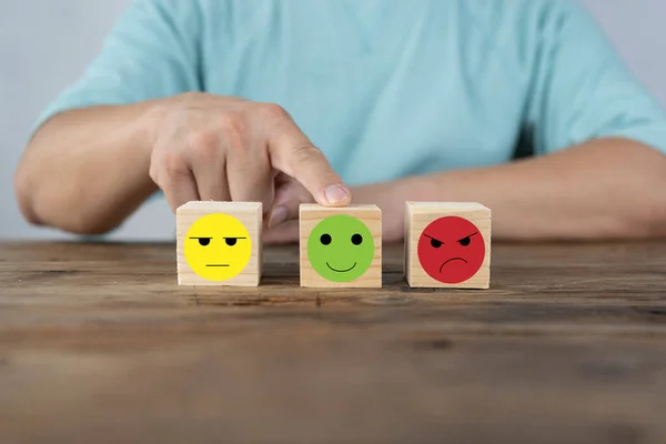 Hand choosing happy smile face wooden block, good feedback rating and positive customer review, mental health assessment, child wellness,world mental health day,think positive, emotional scale concept