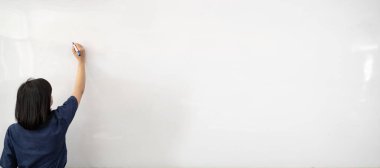 Beyaz tişörtlü bir kadın beyaz arka planda mavi kalemle hayali ekranda yazı yazıyor. Arkadan bak. Yarım boy portre. Öğretmen, ofis çalışanı..