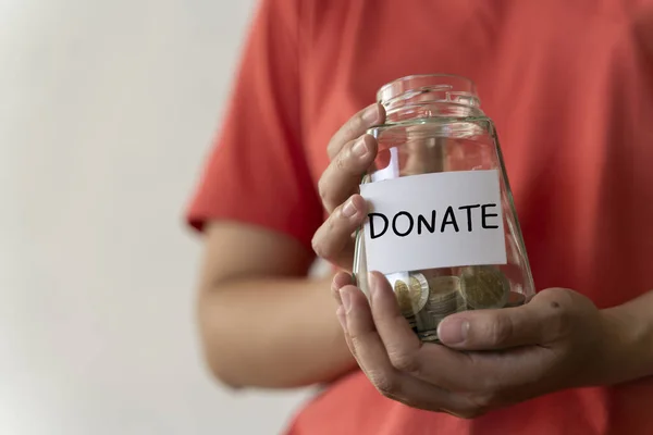 Woman holding money jar with DONATE word written text label for giving and donation concept, saving, fundraising charity, Coronavirus economic stimulus rescue package