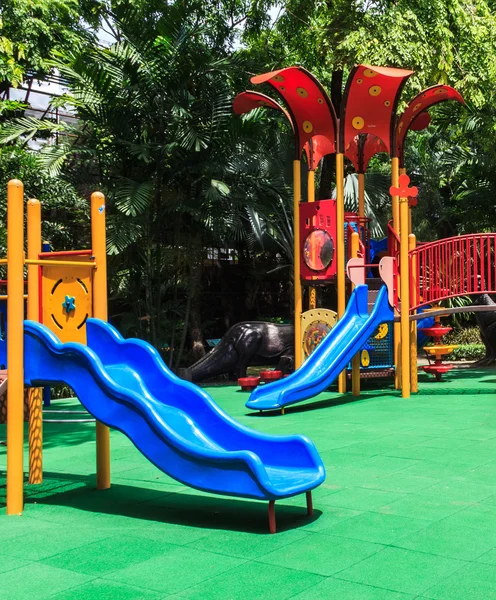 Slides azuis com piso de borracha elástica verde para crianças no parque Fotografias De Stock Royalty-Free